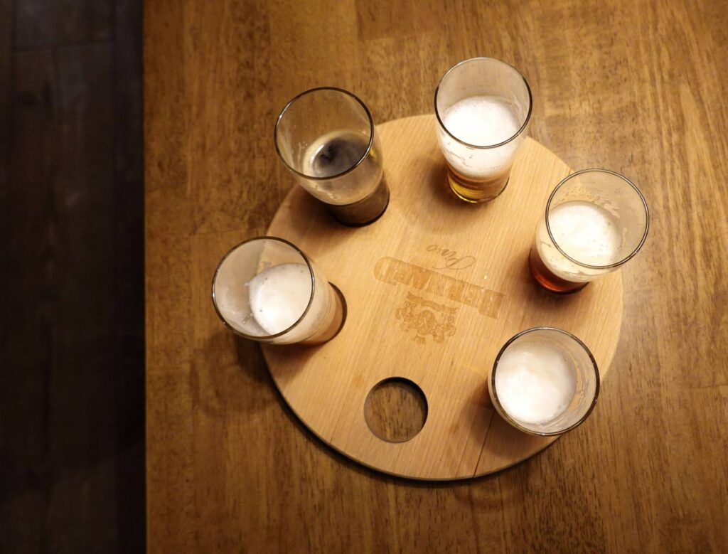 Overhead shot of five beer glasses with foam on a round wooden tray.