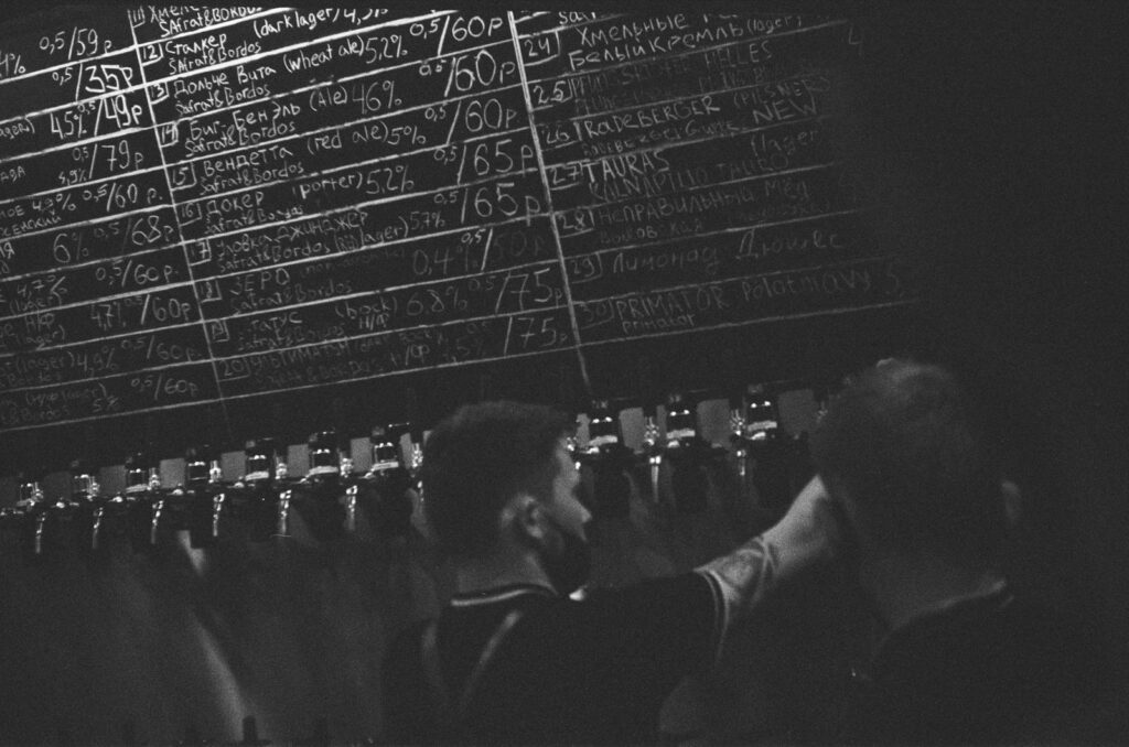 Monochrome view of bartenders working at beer taps in a bar with a chalkboard menu.