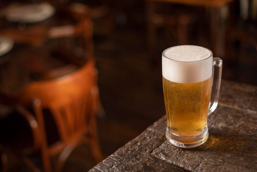 Close-up of a frothy beer mug on a wooden table in a cozy pub setting.